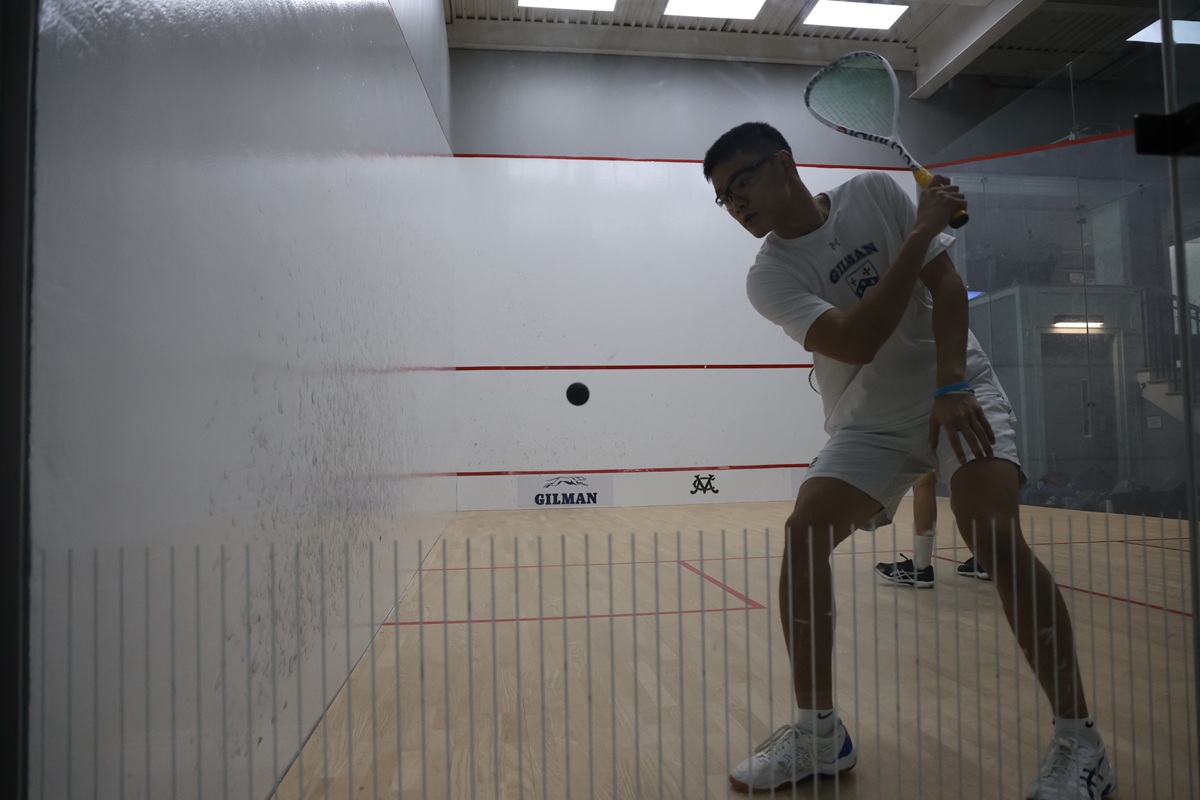 Gilman squash player standing ready in glass court